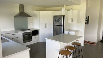 Una cocina moderna con armarios blancos, electrodomésticos de acero inoxidable, una isla central con taburetes y luces colgantes.