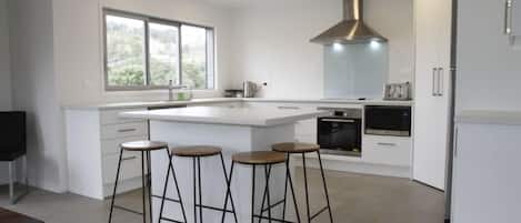 A modern kitchen with a central island, bar stools, a large window, and built-in appliances.