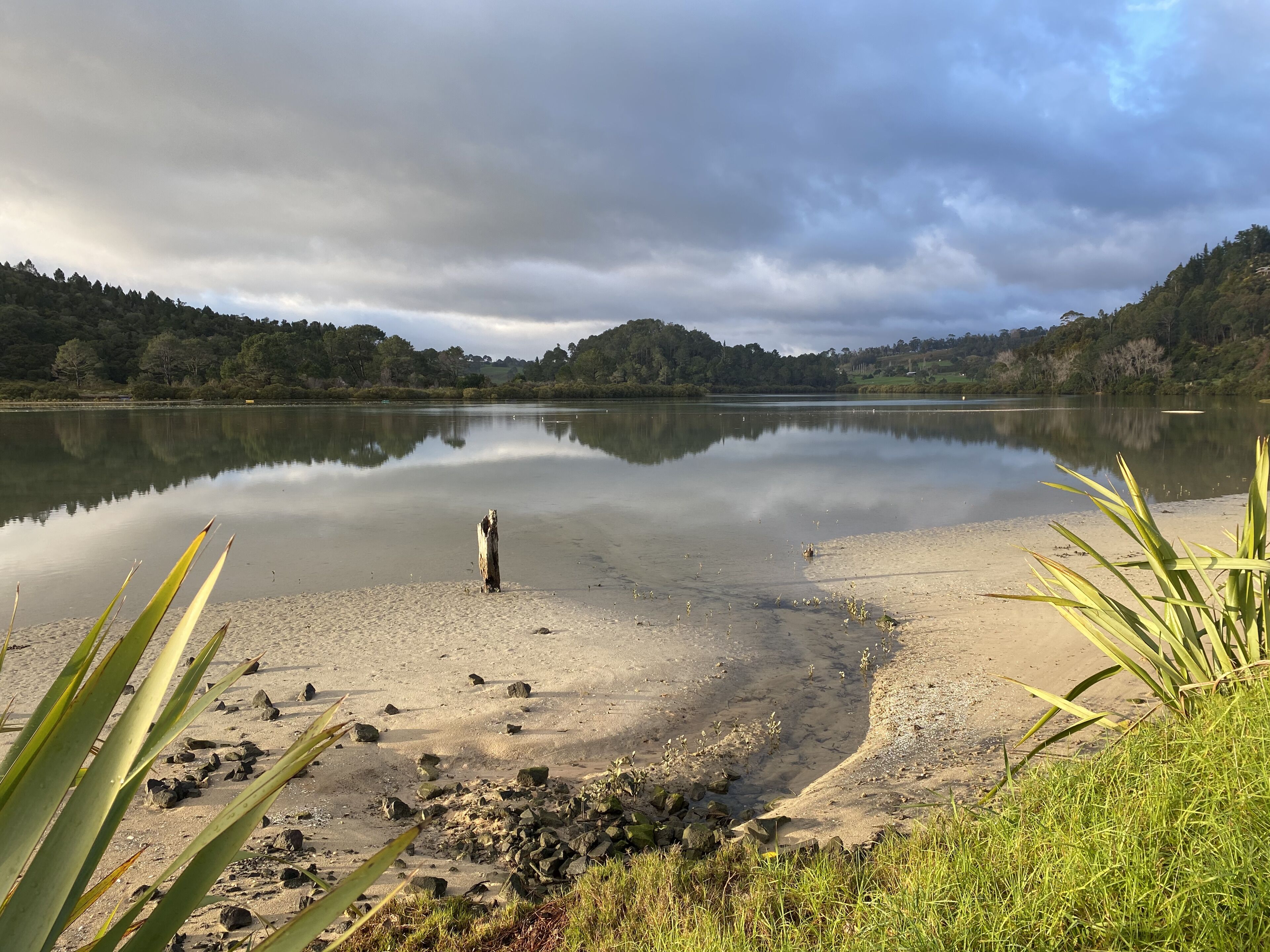 Un lac paisible aux rives sablonneuses, entouré de collines et de végétation.