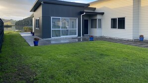 A modern two-story house with a large sliding glass door, a small porch, and a well-maintained lawn. - CooksEstuaryEscape-Waterfront at your doorstep (Price enquire for small groups) (Cooks Beach)