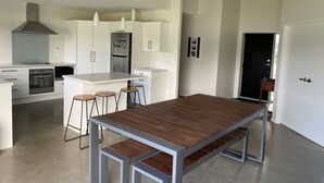 A modern kitchen with white cabinets, a stainless steel refrigerator, a built-in oven, and a large island with bar stools. - CooksEstuaryEscape-Waterfront at your doorstep (Price enquire for small groups) (Cooks Beach)