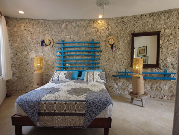 A bedroom with a stone wall, a bed with patterned bedding, a blue headboard, and two wall-mounted lamps.