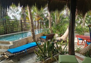 A pool area with lounge chairs and a table, surrounded by palm trees and tropical plants.