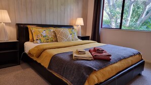 A neatly made bed with a yellow and brown bedspread, two pillows with floral patterns, and a pair of folded towels on the bed. - Ohope Beach  2Brm Weekender escape,handy to beach & more! (Ohope)