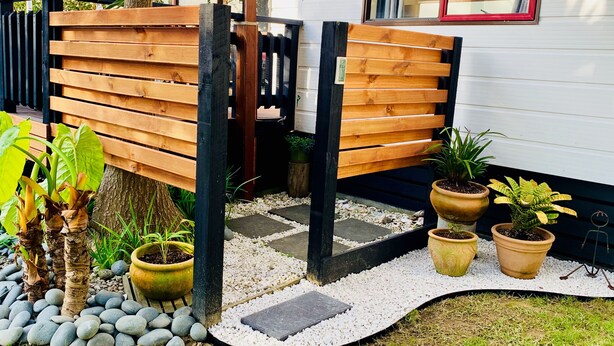 A wooden bench with a black frame, potted plants, and a stone pathway leading to a white building. - Ohope Beach  2Brm Weekender escape,handy to beach & more! (Ohope)