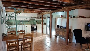 A spacious kitchen with wooden beams, a dining area with a table and chairs, and a living area with a TV and a black chair. - Stylish Stone Cottage with Pool near Fiskardo (Agrilias)
