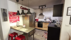 Une cuisine moderne dotée d’un îlot central, d’appareils électroménagers en acier inoxydable et de luminaires suspendus.
