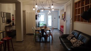 Un salon moderne avec un canapé en cuir noir, un coin repas avec une table et des chaises en bois, et une cuisine visible au fond.
