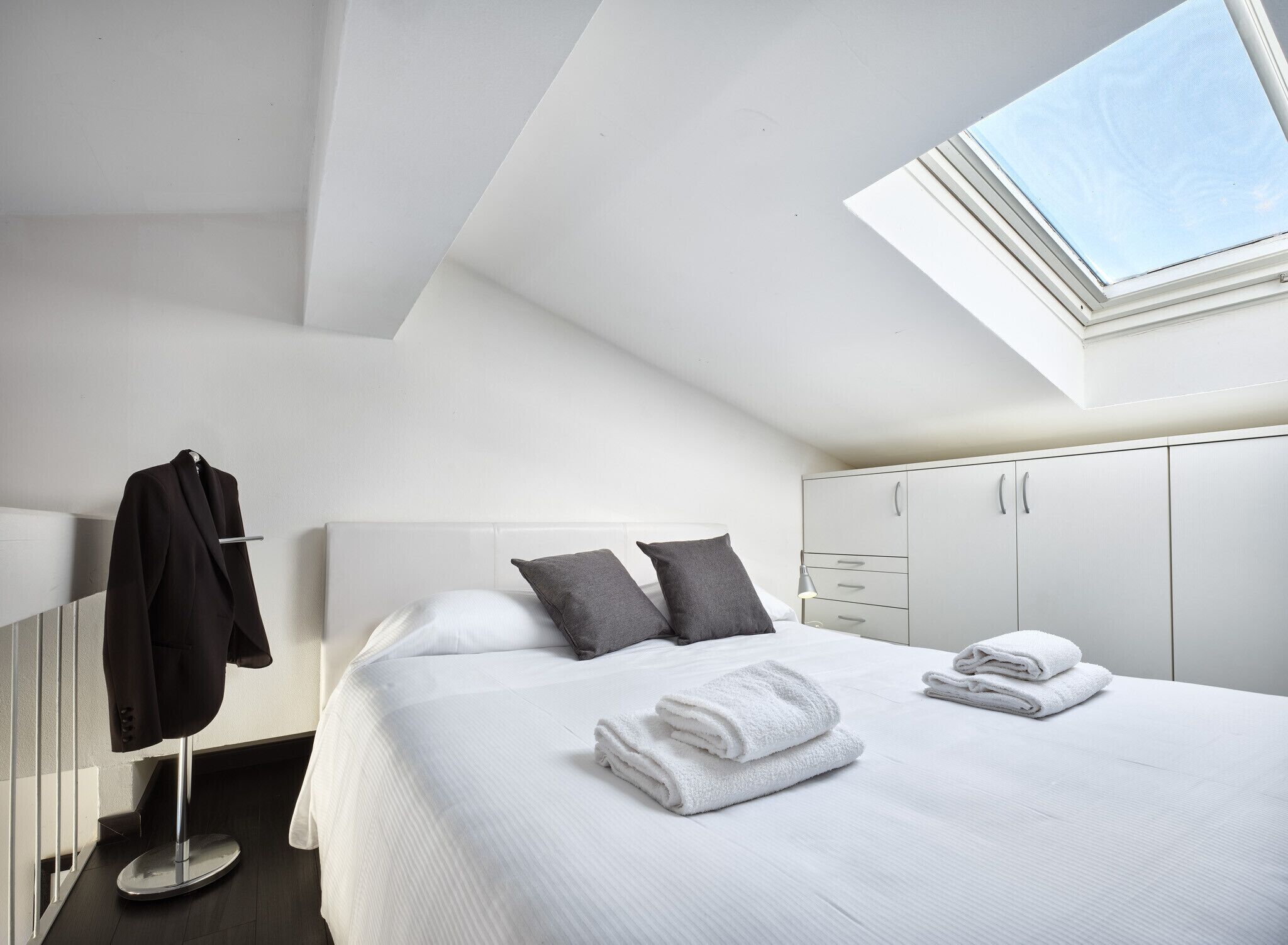 Moderni hotellihuone, jossa on kattoikkuna, siististi pedattu sänky, vaatekaappi ja naulakko.