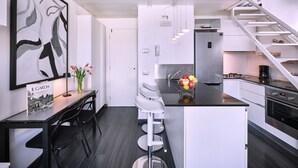 A modern kitchen with a central island, white cabinetry, a stainless steel refrigerator, and a white staircase.