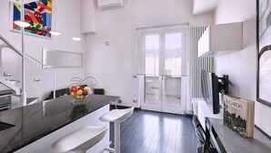 A modern kitchen with a black countertop, white bar stools, a fruit bowl, and a large window with a view.
