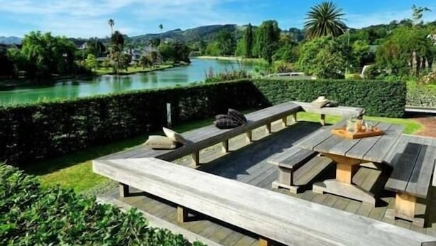 Une terrasse en bois avec des bancs donnant sur un lac, entourée d’une végétation luxuriante et de collines.