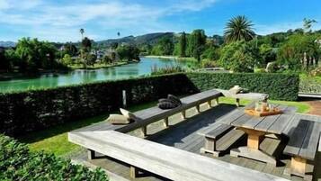 A wooden deck with benches overlooking a lake, surrounded by lush greenery and hills.