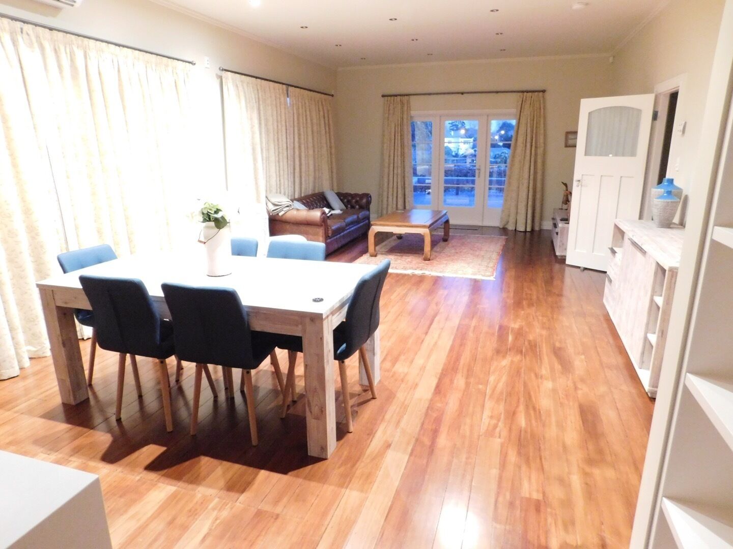 A spacious living area with a wooden floor, a dining table with chairs, a sofa, and a coffee table.