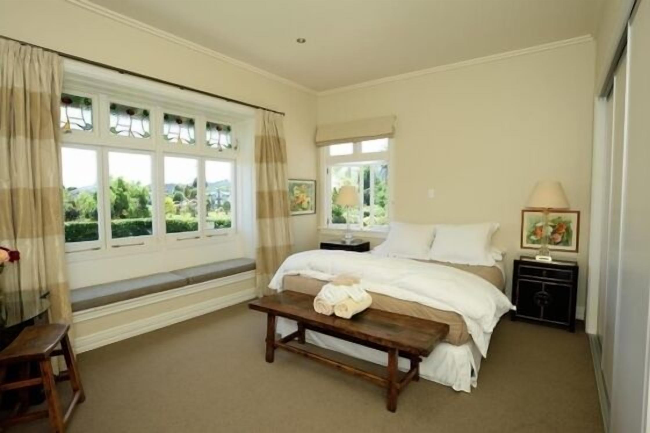 A bedroom with a bed, bedside tables, a bench, and large windows with curtains.