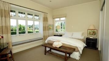 A bedroom with a bed, bedside tables, a bench, and large windows with curtains.