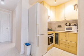 Een kleine keuken met een koelkast, oven, magnetron en gele kastjes.