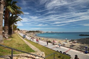 Une promenade en bord de mer offrant une vue dégagée sur la plage et l’océan, avec un chemin pavé et des palmiers.
