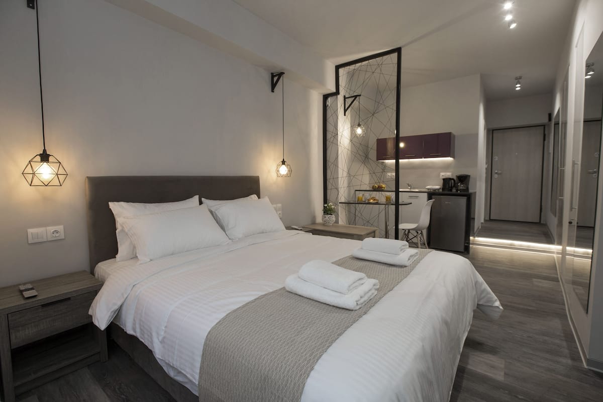 A modern hotel room with a large bed, bedside tables, a nightstand, a desk, a chair, and a mirror.