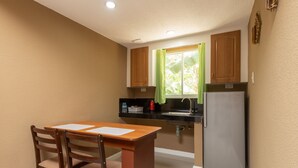 A compact kitchen with wooden cabinets, a sink, a refrigerator, and a dining table with chairs. - Cococabana Panglao (Panglao)