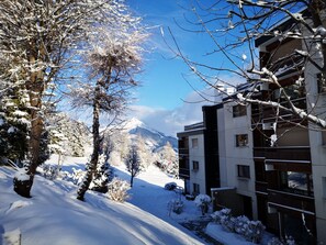 Un paysage enneigé avec un bâtiment moderne doté de nombreux balcons, et une montagne en arrière-plan.