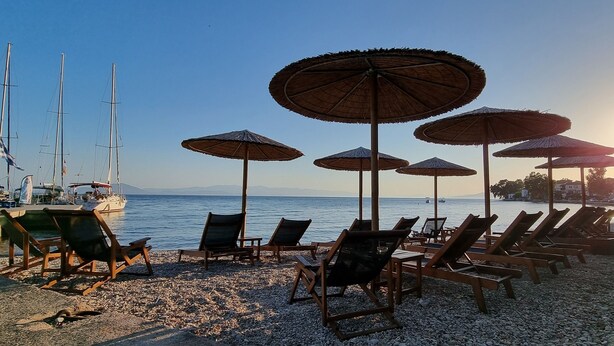 A beach with lounge chairs and umbrellas, a boat docked nearby, and a clear sky.