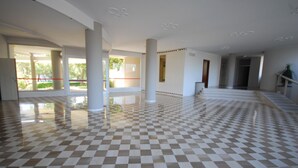 Un vestíbulo espacioso con piso a cuadros, grandes columnas y vista al exterior.