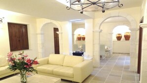 A spacious living area with a cream-colored sofa, a coffee table, and a vase of flowers. There are two archways leading to another room with a dining table and chairs.