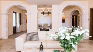 A spacious living room with a beige sofa, a chandelier, and a floral arrangement.