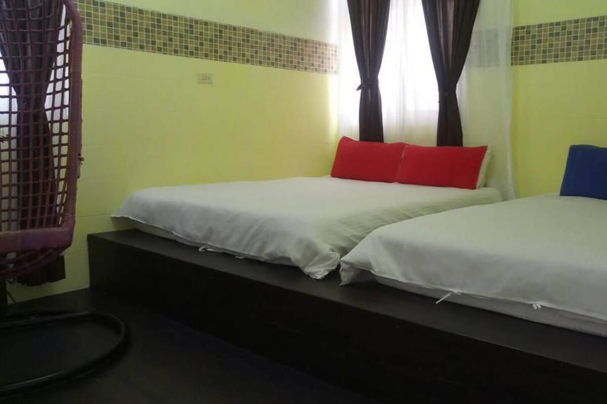 A room with two beds, each with a pillow. There is a chair and a small table.
