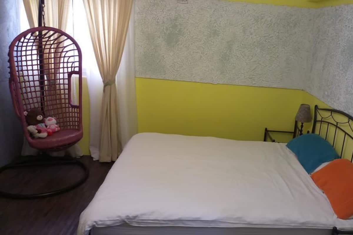 A small, single-bed room with a plain bed, a hanging chair with toys, and a plain wall.