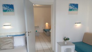 Ein Hotelzimmer mit einem Bett, einem Sofa, einem kleinen Tisch mit einer Vase und einem Flur, der in ein weiteres Zimmer führt.