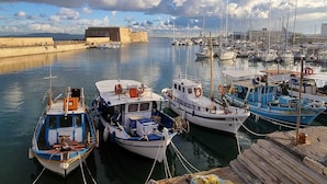Ein Yachthafen mit mehreren vor Anker liegenden Booten, eine Burg im Hintergrund und ein klarer Himmel.