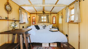 A cozy cabin-style bedroom with a wooden ceiling, a bed with striped bedding, a small table with a vase of flowers, and a bench.