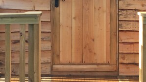 A wooden cabin with a double door, a sign above the door reading "Tinners Warren," and a small window on the upper door.