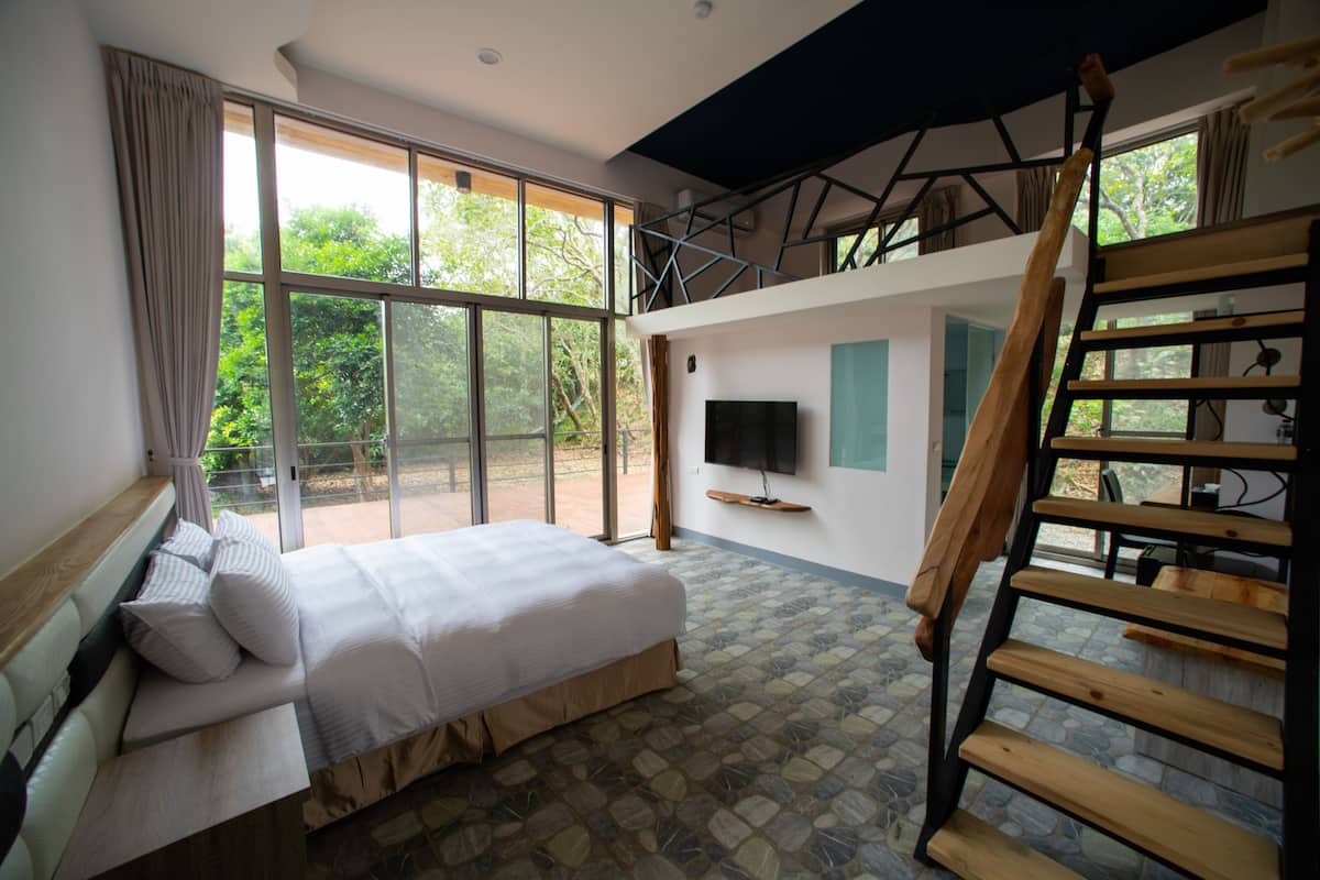 A bedroom with a large bed, a TV, and a wooden staircase.
