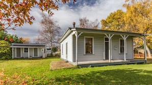 A white, single-story house with a porch and a small attached garage. - Kaha Cottage - Rangataua Holiday Home (Ohakune)