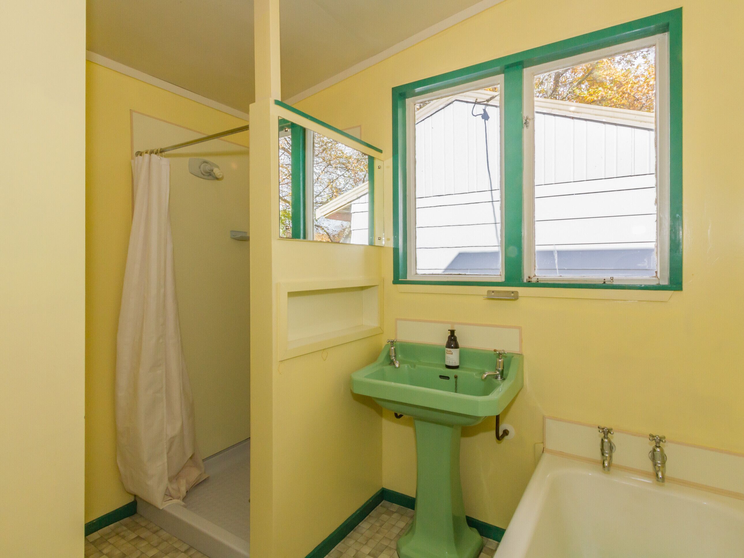 Ein Badezimmer mit einem grünen Waschbecken, einer Badewanne, einer Dusche und einem Fenster mit Blick auf ein Haus.