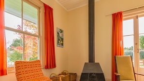 A cozy room with a fireplace, two chairs, a table, and a window with curtains. - Kaha Cottage - Rangataua Holiday Home (Ohakune)