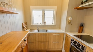 A kitchen with wooden cabinets, a stainless steel sink, a window, and a built-in oven. - Kaha Cottage - Rangataua Holiday Home (Ohakune)