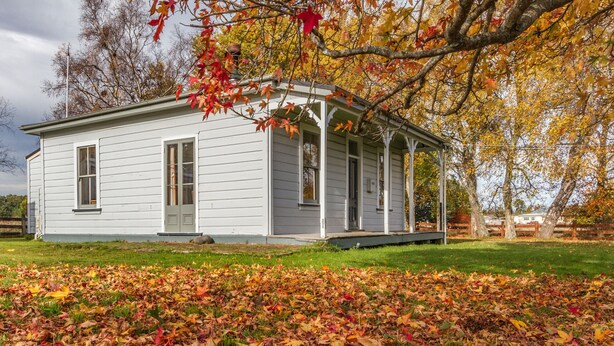 A white wooden house with a porch, surrounded by fallen autumn leaves. - Kaha Cottage - Rangataua Holiday Home (Ohakune)