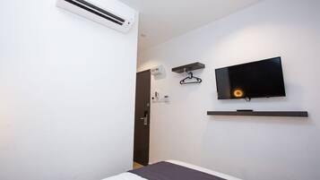 Habitación de hotel con cama, televisor montado en la pared, aire acondicionado instalado y una puerta.