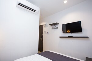 Habitación de hotel con cama, televisor montado en la pared, aire acondicionado instalado y una puerta.