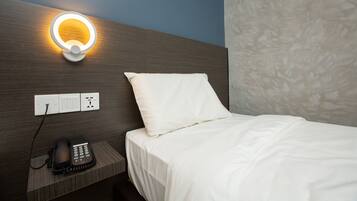 Una habitación de hotel con una cama, un teléfono en la mesita de noche y una lámpara de pared.