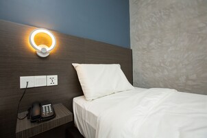 Una habitación de hotel con una cama, un teléfono en la mesita de noche y una lámpara de pared.