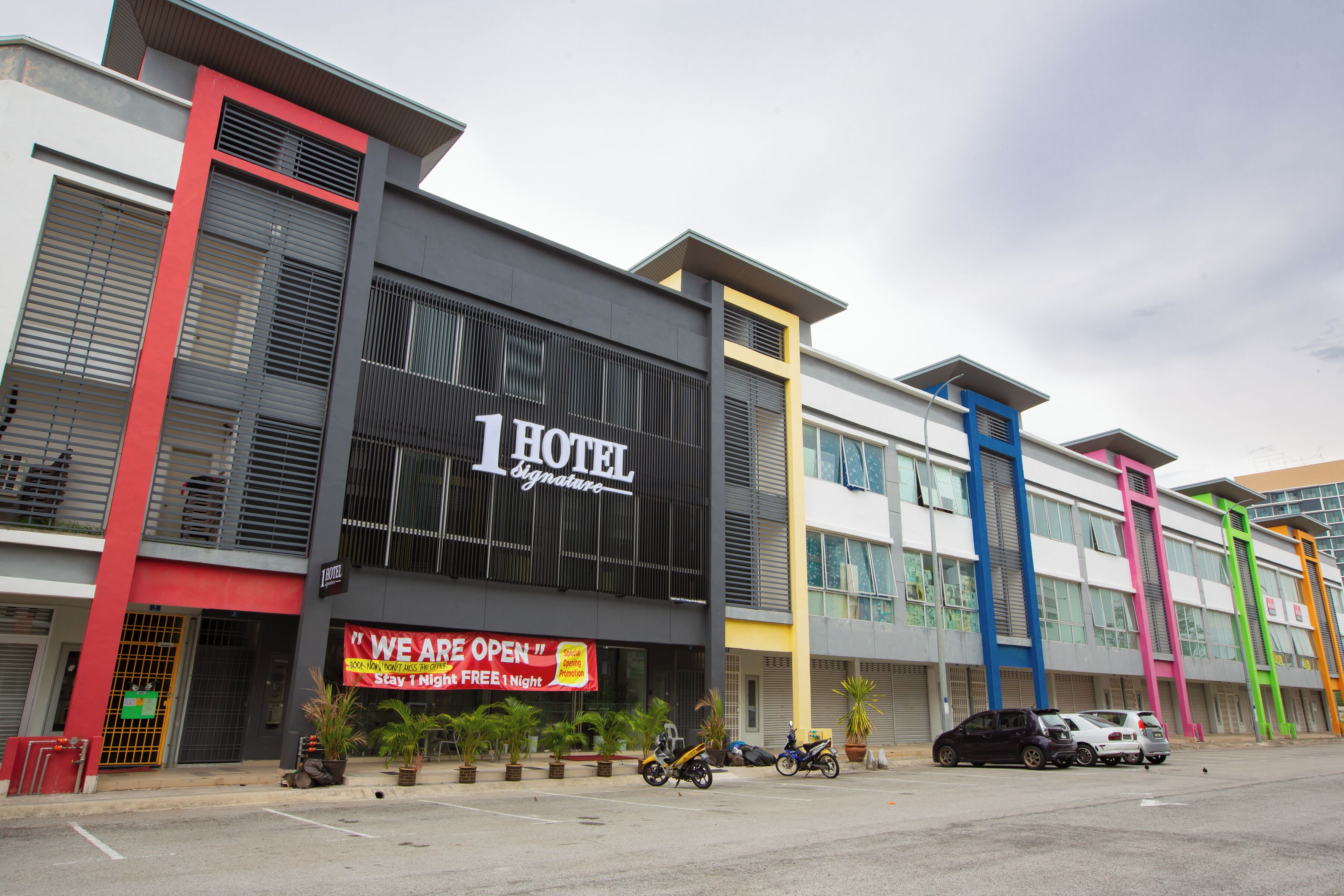 A hotel with a prominent '1 Hotel Signature' sign, a 'We Are Open' banner, and several parked vehicles including motorcycles and cars.