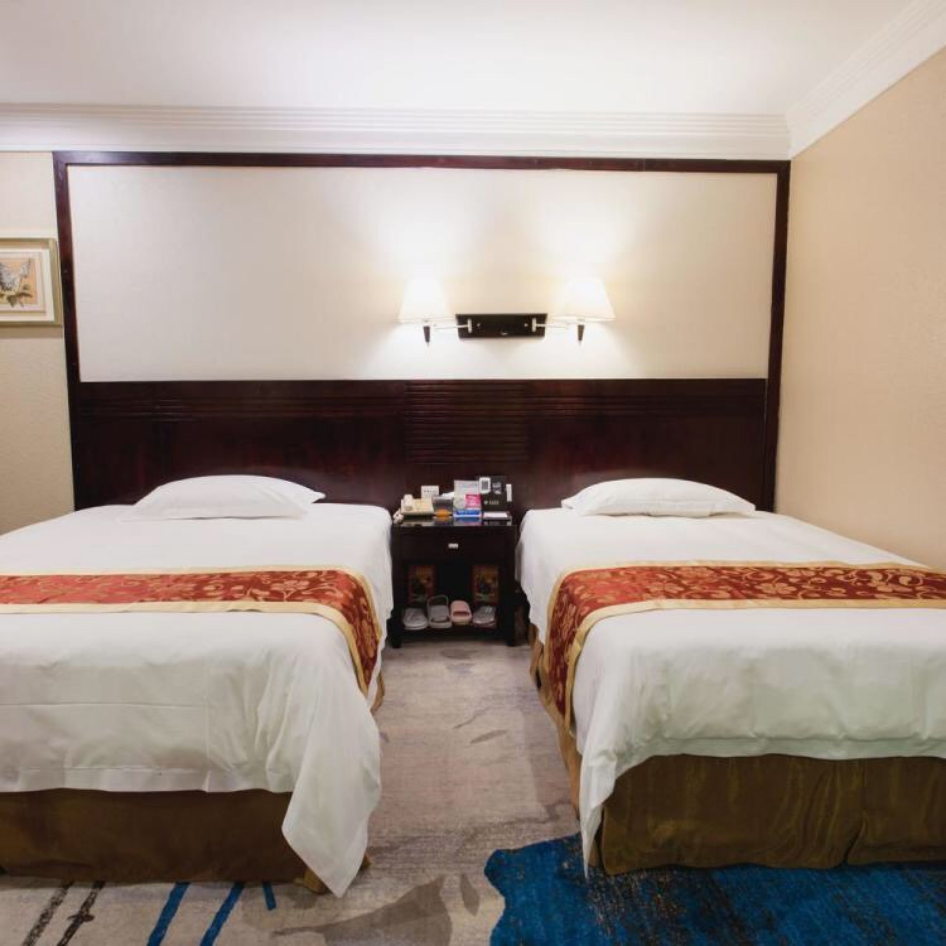 A hotel room with two beds, a nightstand, a lamp, and a carpeted floor.