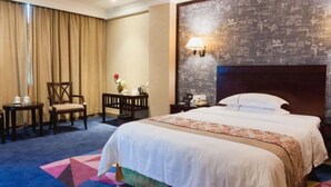 A hotel room with a large bed, a desk, a chair, a nightstand, and a wall with a decorative light fixture. - Mizparton Hotel (Foshan)