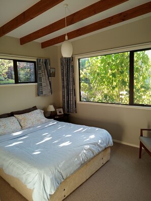 A bedroom with a bed, a nightstand, a chair, a window with curtains, and a view of greenery outside.