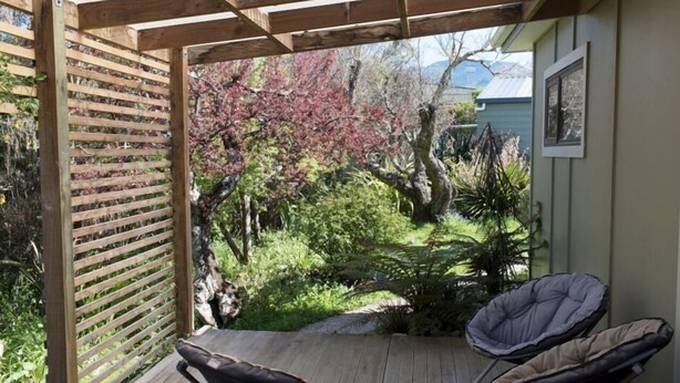 A wooden deck with two cushioned chairs, surrounded by a garden with various plants and trees.